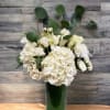White flowers arranged in a tall green vase with round eucalyptus stems