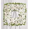 White floral wreath on a black easel with lilies and daisies