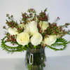 White roses and pink filler flowers arranged in a glass vase