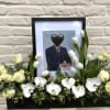 White floral tribute around a framed portrait in a black container.