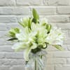 White lilies in a clear glass vase with a silver ribbon