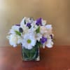 White and purple mixed flower arrangement in a square glass vase