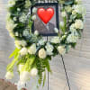White floral funeral wreath on an easel with a framed photo in the center