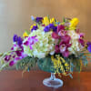 Mixed bouquet in a glass compote vase with purple, yellow, and white blooms