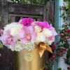 Pink orchids and white roses in a gold hatbox with a ribbon