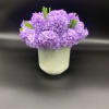 Purple flower arrangement in a pale green cylindrical vase