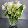 White roses and green orchids arranged in a clear glass vase
