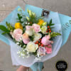 Hand-tied bouquet of pastel roses and mixed flowers wrapped in light blue paper