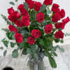 Tall arrangement of long-stemmed red roses in a clear glass vase with striped ribbon