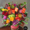 Large colorful arrangement of roses, hydrangeas, protea and mixed blooms in a pink vase on a wood slice