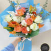 Hand-tied bouquet of peach and white roses with orange lilies and white blooms in blue wrapping.