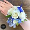 White rose and blue flower wrist corsage with ribbon on a person’s wrist