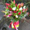 Tall arrangement of red, pink, white, and peach tulips in a striped vase with ribbons