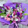 Hand-tied bouquet of pink and purple flowers with white calla lilies wrapped in purple paper.