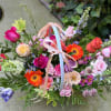 Colorful basket arrangement of pink roses, orange gerbera daisies, and mixed blooms with pastel ribbon bows