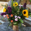 Bouquet with sunflowers, purple lilacs, and pink roses in a burlap-wrapped vase