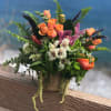 Mixed bouquet with orange roses and purple orchids in a burlap-wrapped container