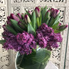 Purple tulips and lilac blooms arranged in a clear glass vase