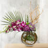 Purple orchids and hydrangeas in a glass vase with palm fronds and branches