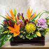 Tropical floral arrangement with orange and purple blooms in a rectangular vase
