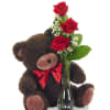 Teddy bear holding a vase of red roses and small white flowers