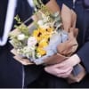 Handheld bouquet of yellow and white flowers wrapped in brown paper