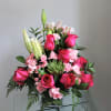 Pink roses and lilies arranged in a clear vase with greenery.