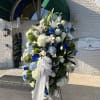 Large funeral spray of white, blue, and green flowers on an easel
