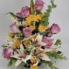 Arrangement of pink roses, yellow chrysanthemums, and white lilies in a low black container