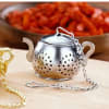 Metal tea infuser with a chain and lid on a wooden surface
