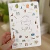 Hand holding a white notebook with small illustrated objects and the words "living freely and lightly"