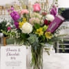 Tall mixed bouquet in a glass vase with a chocolate bar tucked in.