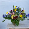Mixed bouquet in a clear glass vase with blue, yellow, pink, and purple flowers.