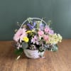 Pastel mixed flower arrangement in a white basket with a handle