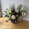 White floral arrangement in a dark vase with a central protea and rose