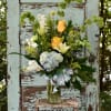 Bouquet of yellow roses, hydrangea, and white lilies in a glass vase