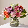 Bouquet of pink lilies, orange roses, and purple flowers in a glass vase