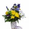 Mixed yellow, white, and blue flowers in a white container with a small gift box