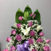 Pink roses and white lilies arranged with baby's breath and a purple ribbon