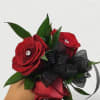Handheld bouquet of red roses with black ribbon and green leaves