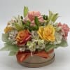 Mixed roses and lilies arranged in a round gift box with an orange ribbon
