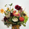 Mixed bouquet in a bark-covered container with burgundy, peach, white, and green flowers