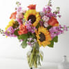 Mixed bouquet with sunflowers, roses, and pink flowers in a glass vase