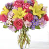 Bouquet of pink roses, yellow lilies, and purple daisies in a glass vase