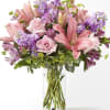 Pink lilies and roses arranged in a clear glass vase with purple flowers
