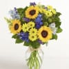 Bouquet of sunflowers, yellow daisies, and blue flowers in a glass vase