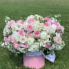 Pink and white floral arrangement in a pink box on grass