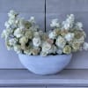 White roses and cream flowers arranged in a white bowl vase