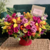 Colorful mixed flower arrangement in a red vase on a wicker table