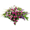 Casket spray of pink roses, white lilies, and purple flowers in a low, elongated design